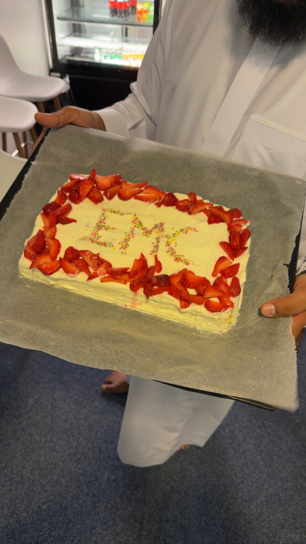 A cake decorated with strawberries and the letters "EMC" in icing, held at an EMC business lounge event