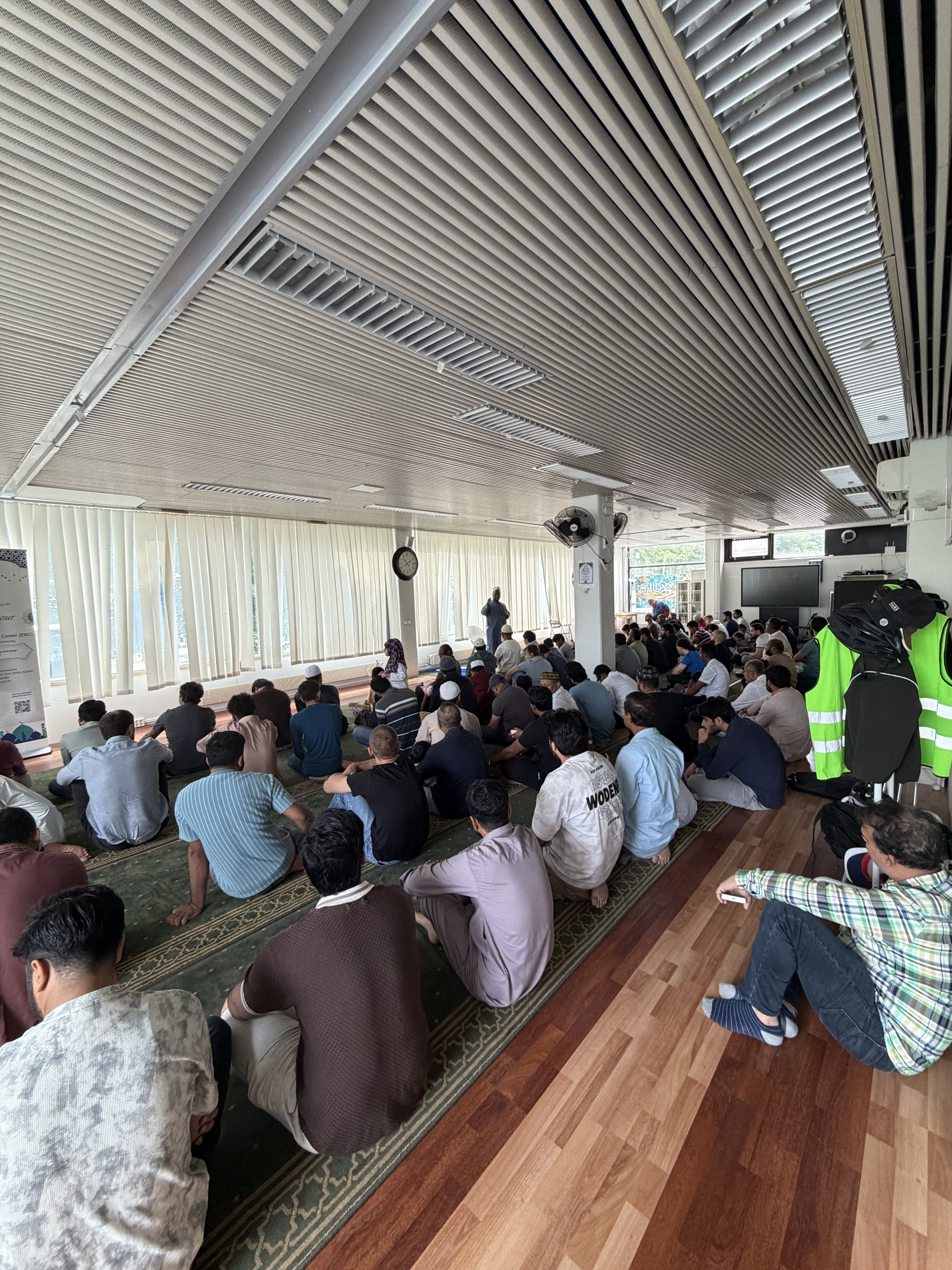 A large indoor congregation seated on the floor listening to a talk at EMC